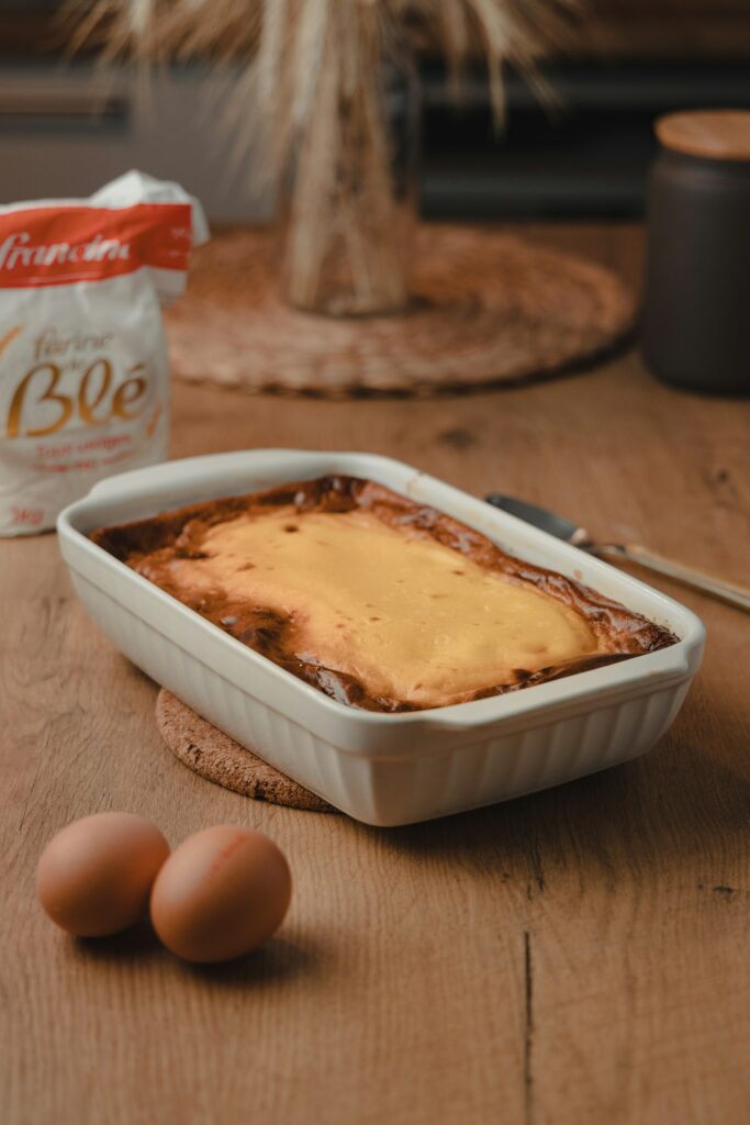 A golden baked egg dish in a white rectangular baking dish with two brown eggs on the table