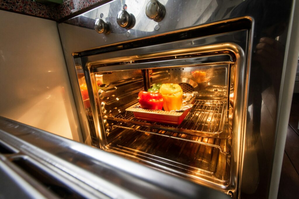 An open oven with its light on and peppers roasting in a dish on the rack
